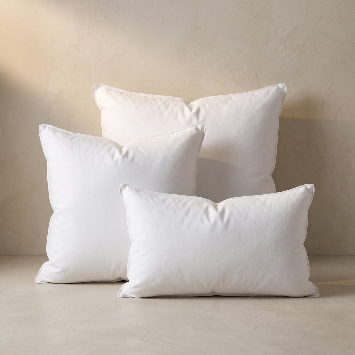 Three white pillow inserts: a 24-inch square, a 20-inch square and a 12x20 lumbar, against a plaster wall